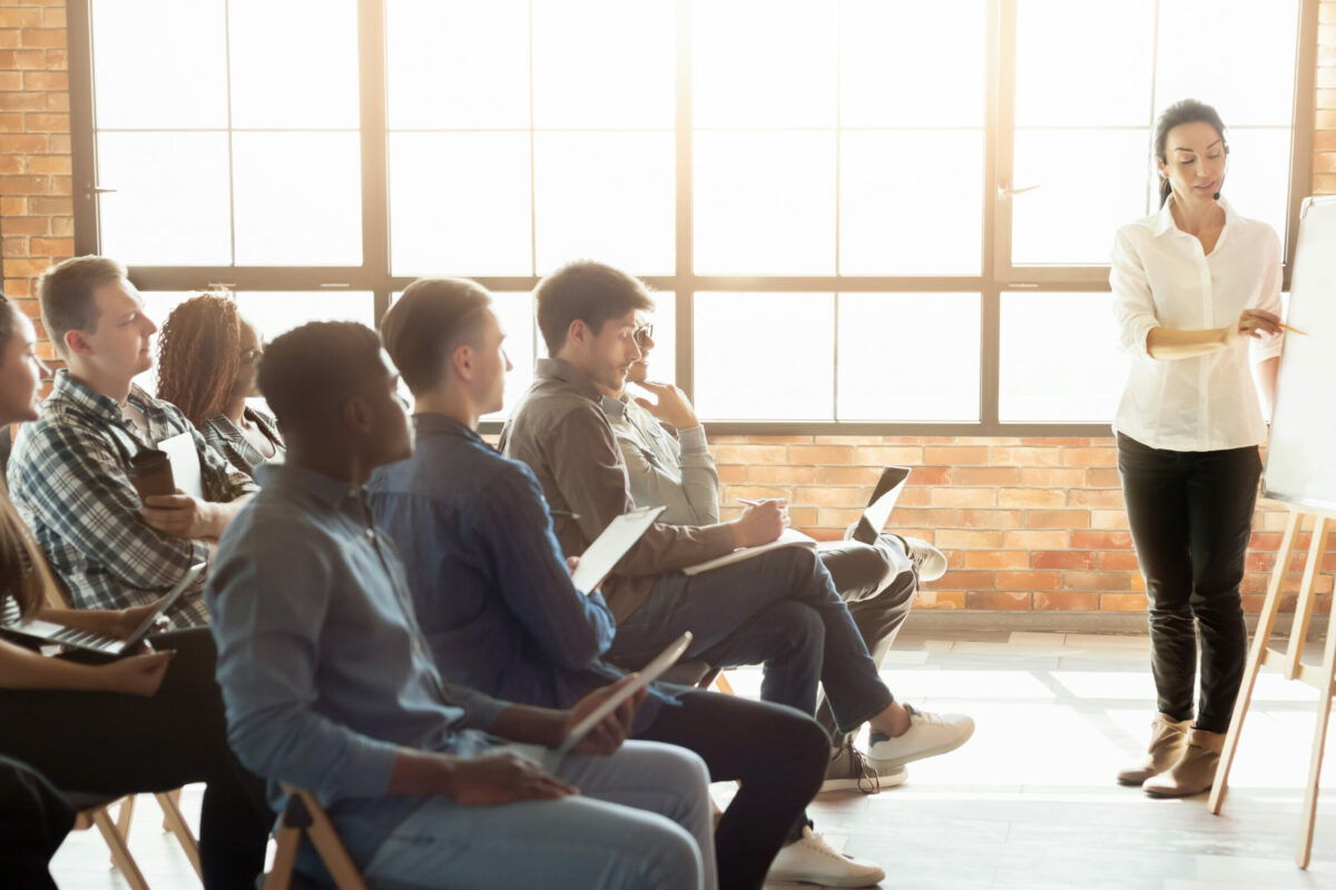 Frau stellt etwas einer Gruppe junger Personen vor