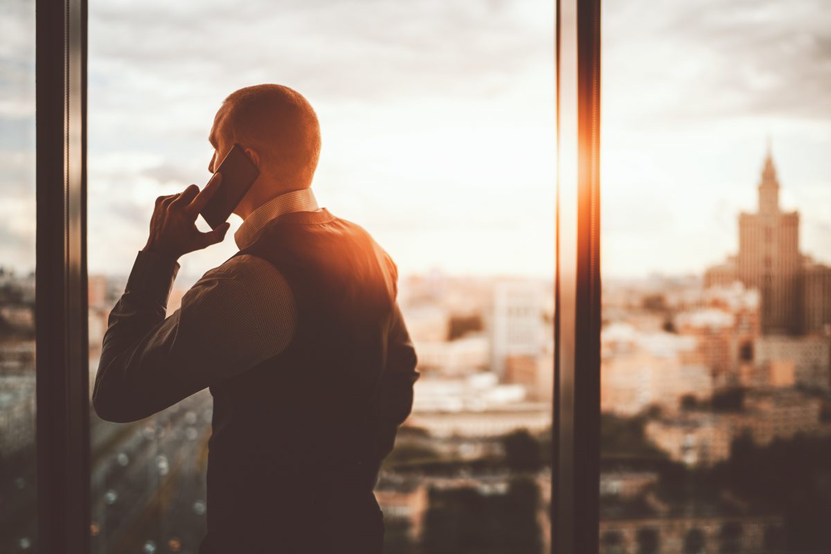 ein Mann telefoniert und schaut aus dem Fenster über eine Stadt